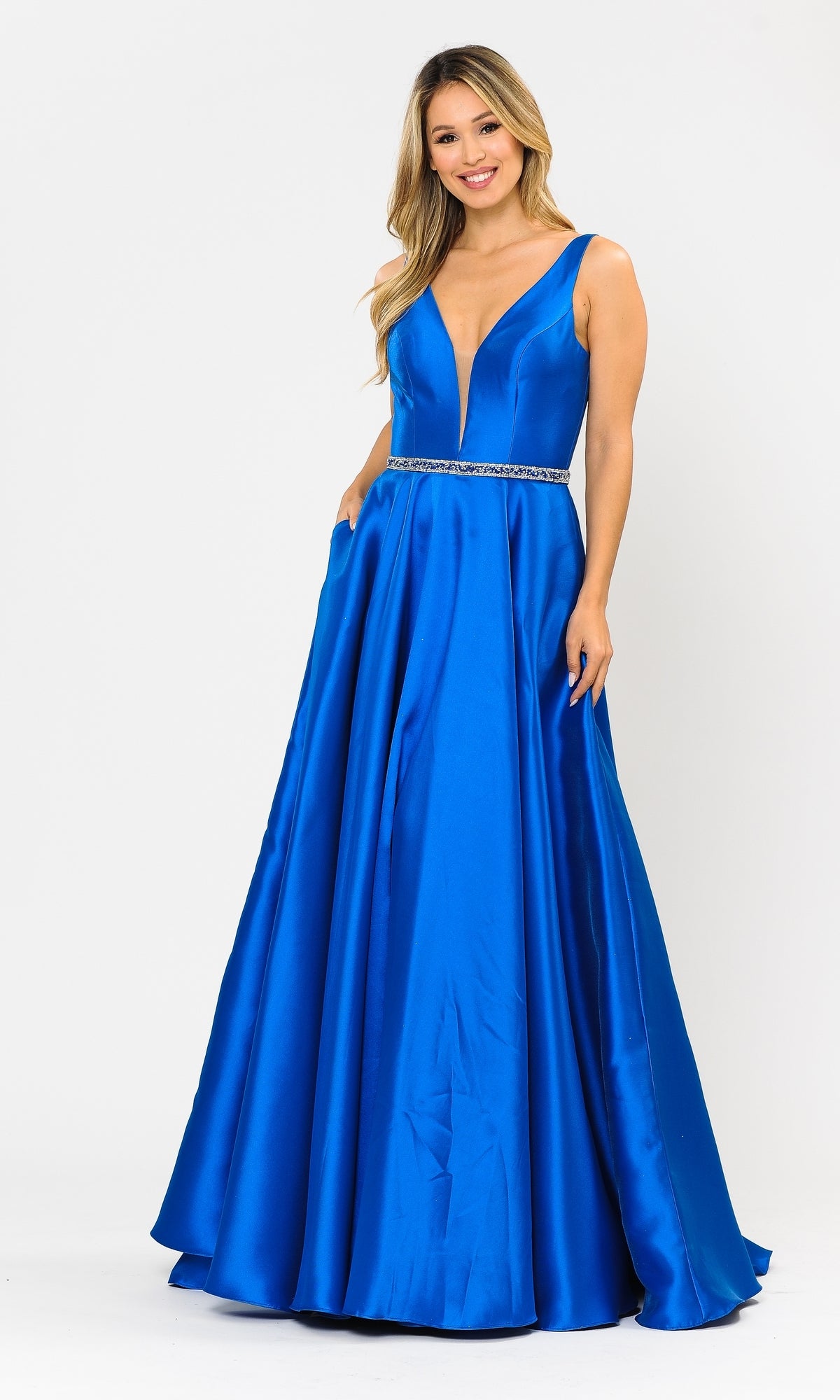A woman stands against a white background wearing the Deep V-Neck Long Mikado A-Line Prom Dress 8682, a sleeveless, floor-length royal blue gown with a deep V-neckline and jeweled waistband.